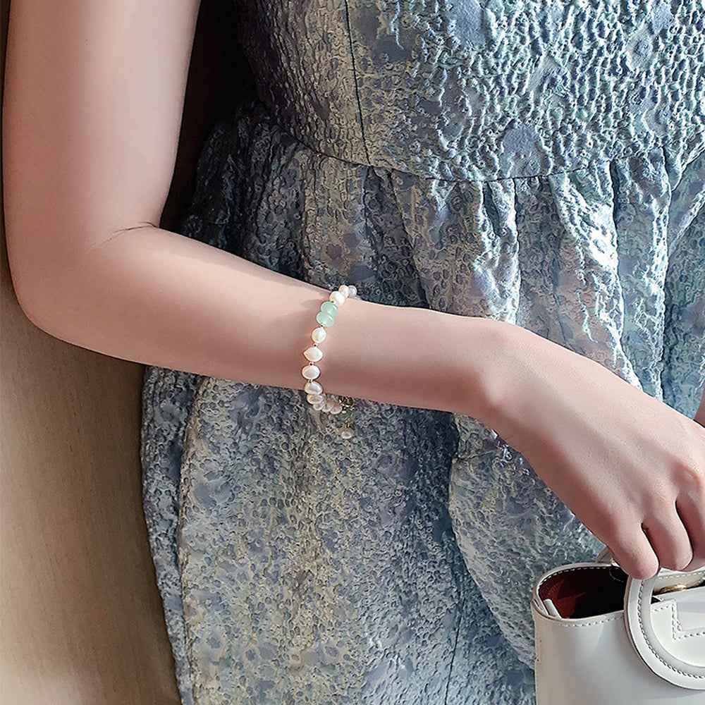 Pearl bracelet worn on wrist with white beads and small green charm