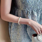 Pearl bracelet worn on wrist with white beads and small green charm