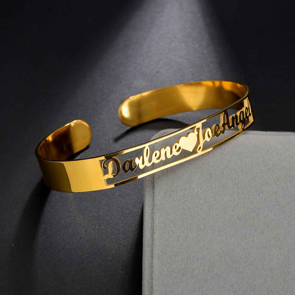 Gold stainless steel cuff bangle with engraved cursive name and open-heart cutout details