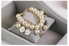 Gold-tone pearl charm bracelet with coin medallions, white flower, blue enamel flower, and horse dangle