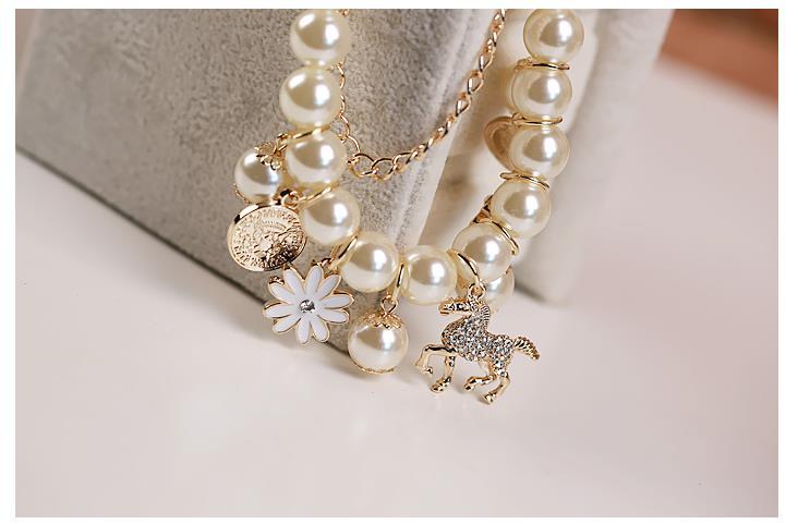Pearl and gold-tone charm bracelet with stacked pearls, white flower, coin and horse charms