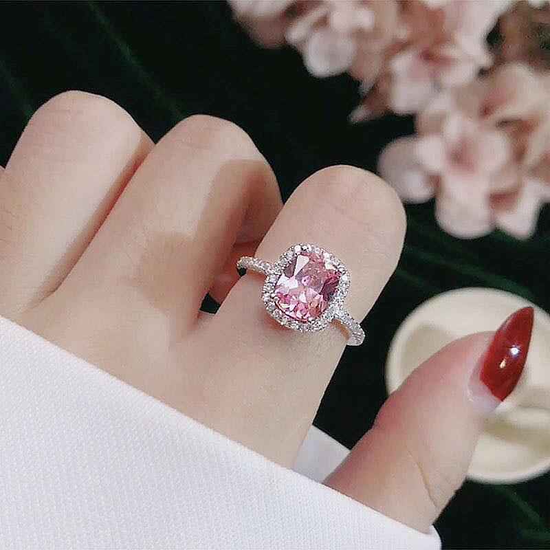 Silver-toned ring set with oval pink center stone and halo, worn on hand
