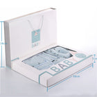 Open baby gift box with light blue baby clothing folded inside, shown in foam tray