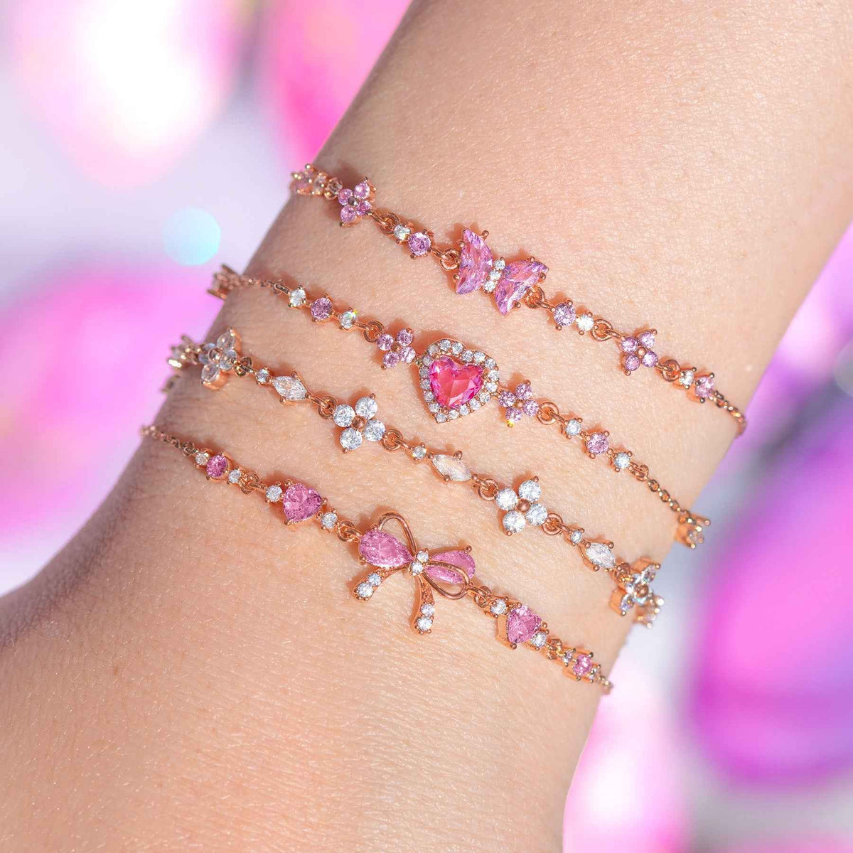 Three gold-tone rhinestone bracelets on wrist with pink hearts and bow charms