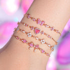 Three gold-tone rhinestone bracelets on wrist with pink hearts and bow charms