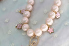 Pink pearl necklace with star and butterfly charms along a gold-tone clasp