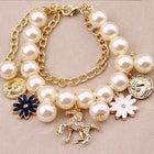 Gold-tone pearl charm bracelet with blue flower, white flower, and horse coin dangles