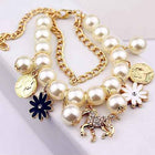 Gold-tone pearl charm bracelet with coin medallions, white flower, blue enamel flower, and horse charm