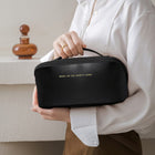 Black travel cosmetic bag with zip closure, held in hand over a tabletop