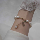 Gold-tone pearl bracelet on wrist with green zircon, tag charm, and pearl dangle
