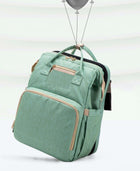 Foldable baby travel bed backpack in green with front pockets and carry handles.