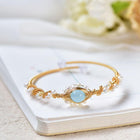 Gold cuff bracelet with braided wire, white pearls, and a blue oval centerpiece