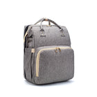 Grey foldable baby travel bed backpack with front zip pocket and gold-tone hardware.