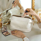 White cosmetic bag with zip closure and gold-tone accents, compact crossbody style