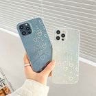 Blue transparent iPhone case with colorful hearts beside cream heart case, camera cutouts