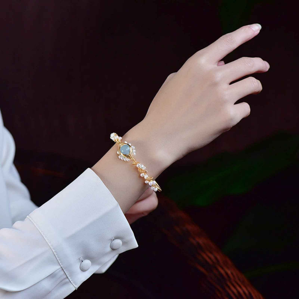 Gold pearl cuff bracelet on wrist with braided chain and blue oval charm