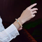 Gold pearl cuff bracelet on wrist with braided chain and blue oval charm