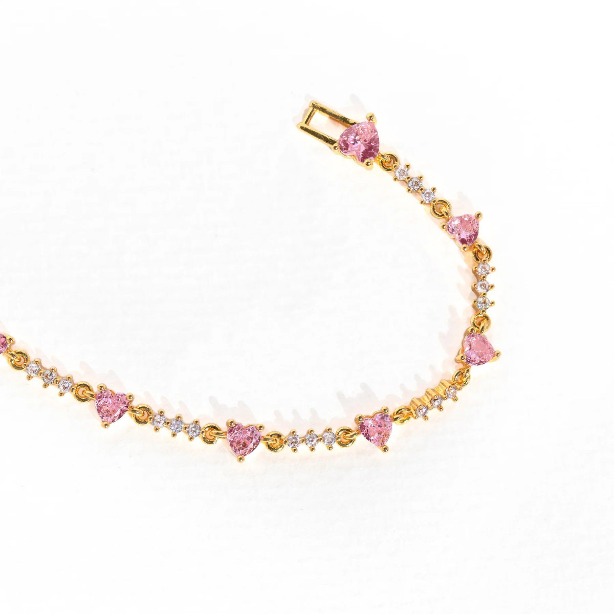 Gold chain bracelet with pink heart charms and rhinestone bow-like detail