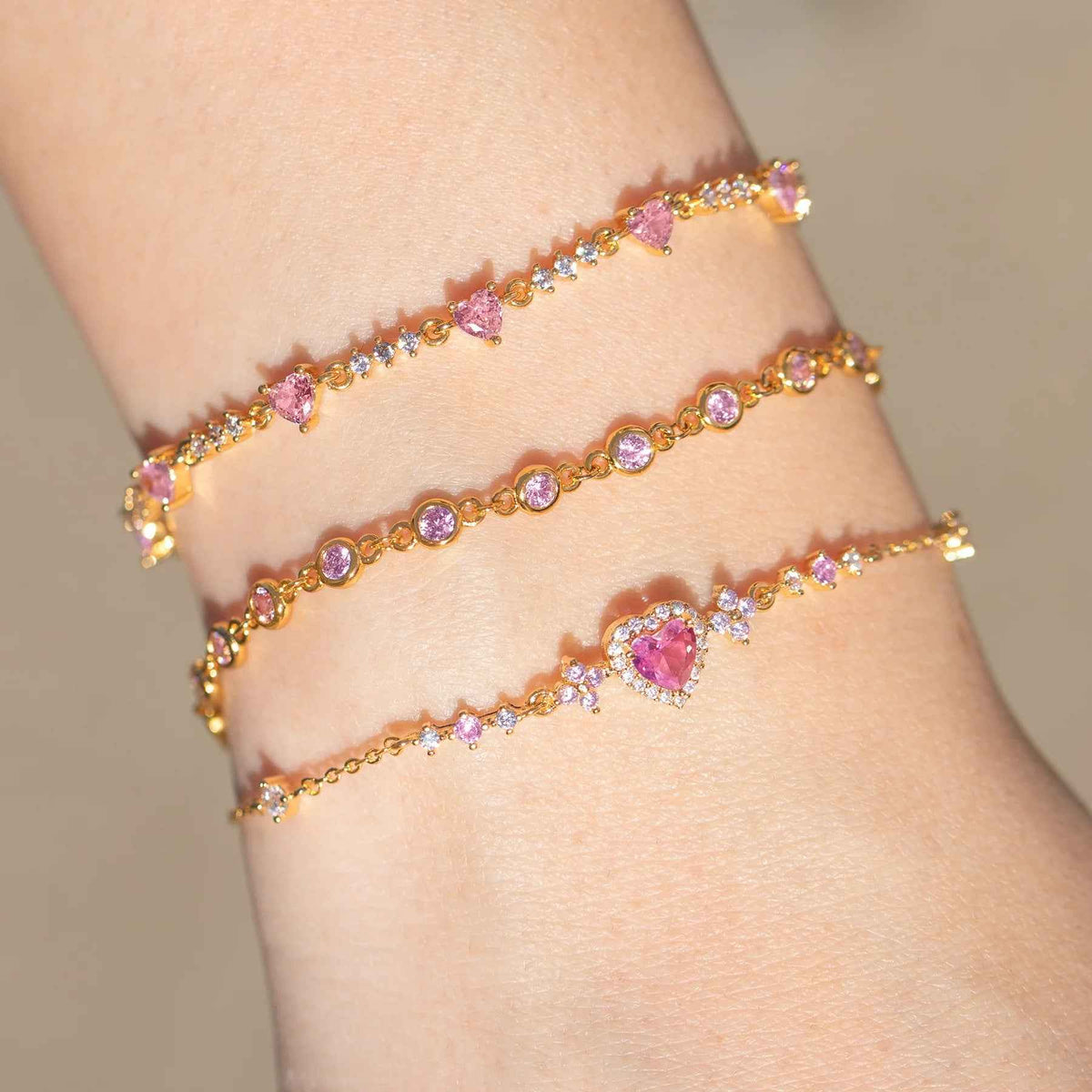 Stacked gold-tone rhinestone bracelets with pink heart charms and bow detail