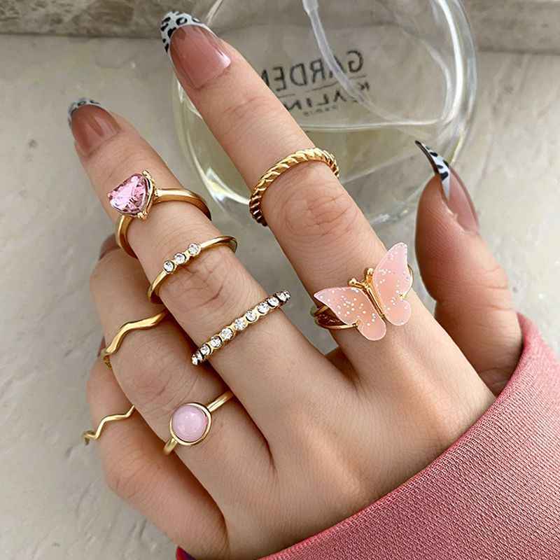 Gold boho stacking rings set with pink gemstone and butterfly charm, plus crystal bands