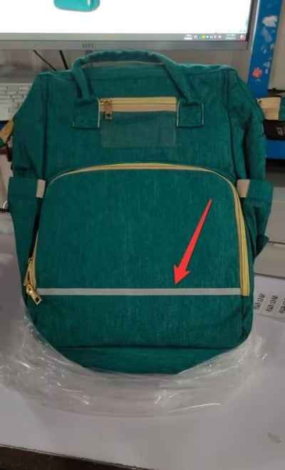 Green baby travel bed backpack with beige trim and zippered front panel; red arrow marker