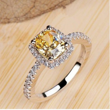 Silver-toned ring set with oval yellow center stone and halo, on wood surface