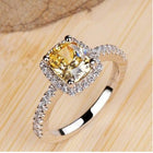 Silver-toned ring set with oval yellow center stone and halo, on wood surface