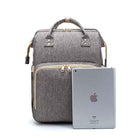 Grey foldable baby travel bed backpack with front zip pocket, holding a tablet device.