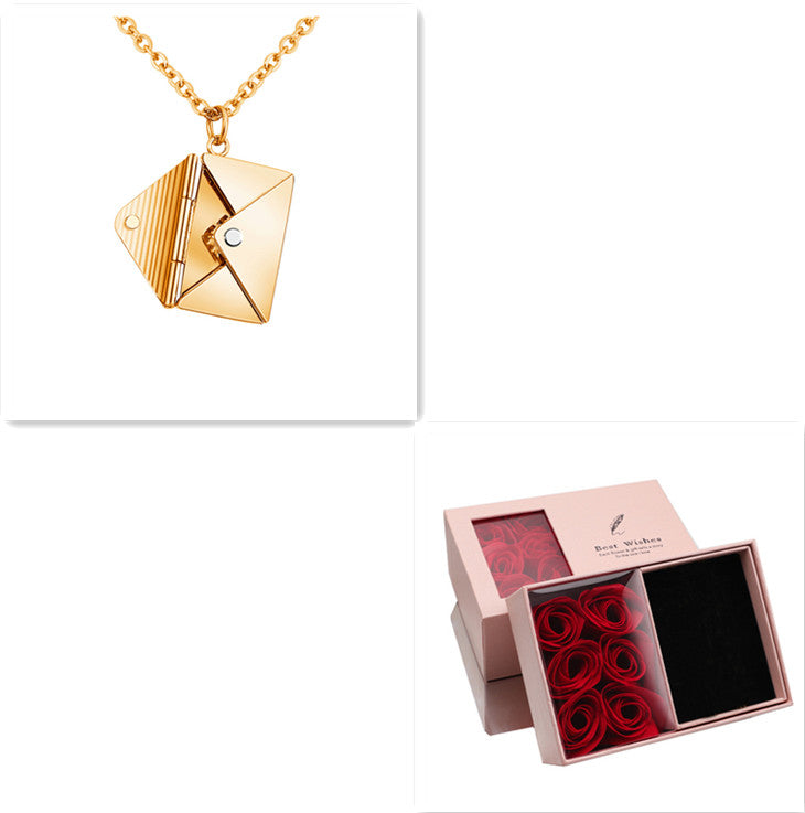 Gold envelope pendant necklace shown with gift box and red rose decor