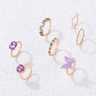 Gold geometric ring set with purple gemstone, star charm, and butterfly open bands
