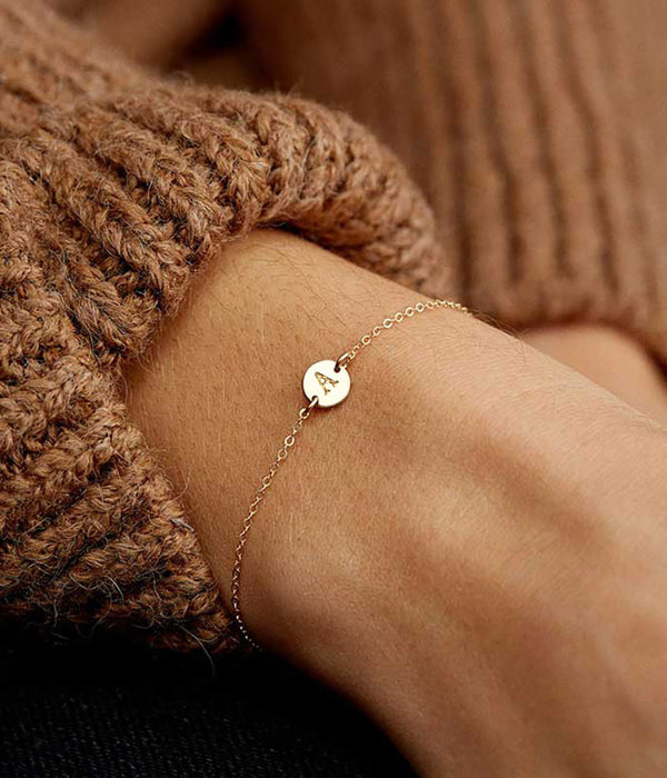 Gold-tone bracelet on wrist with small round charm and adjustable chain links