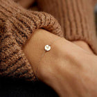 Gold-tone bracelet on wrist with small round charm and adjustable chain links