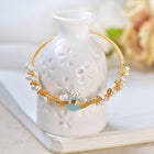 Gold braided pearl cuff bracelet with white bead details and a blue oval center