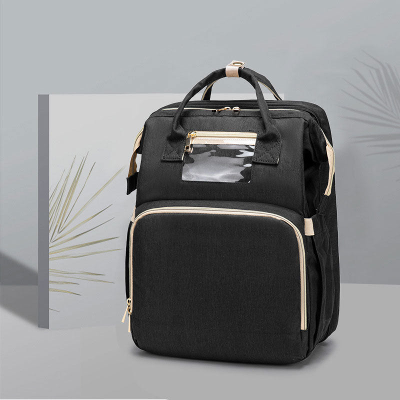 Black foldable baby travel bed backpack with gold trim, front zip pocket, and handles.