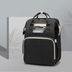 Black foldable baby travel bed backpack with gold trim, front zip pocket, and handles.