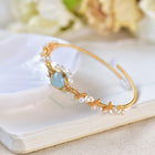 Gold wire cuff bracelet with white pearls, braided accents, and a blue oval charm