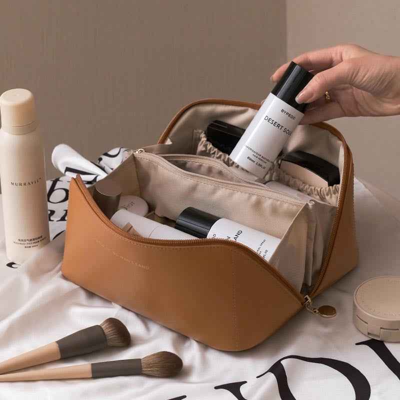 Tan travel cosmetic bag opened with zip top, inner divider pockets visible