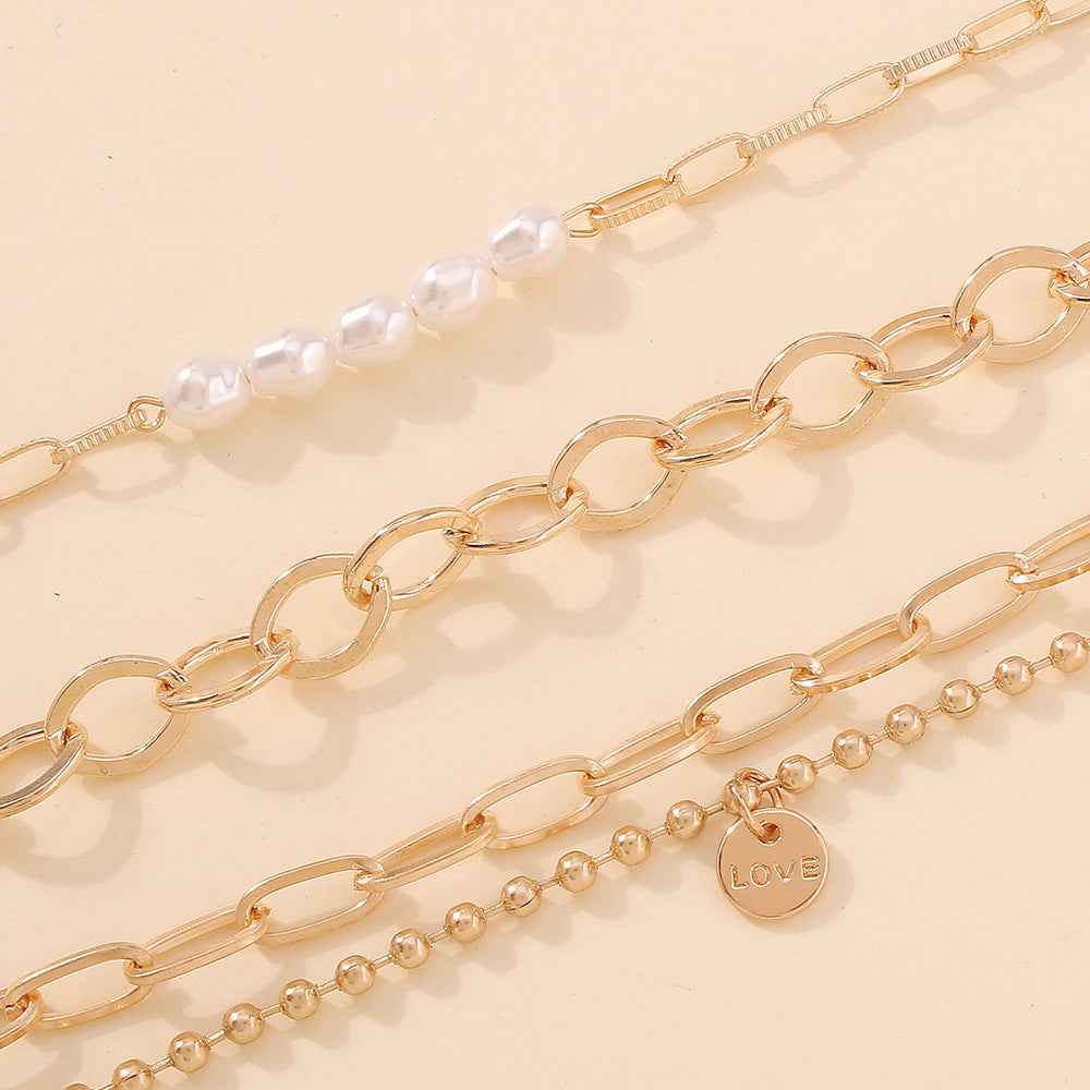 Close-up gold-tone chain bracelet with oval links, pearl beads, and 'love' charm