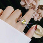 Silver-toned ring set with oval yellow center stone and halo, worn on hand