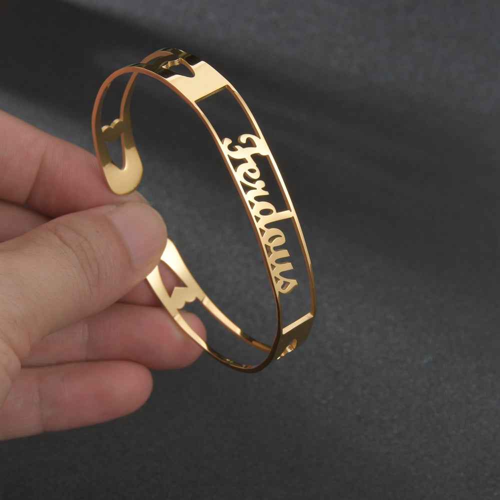 Gold stainless steel cuff bracelet held in hand; engraved cursive name on slim band