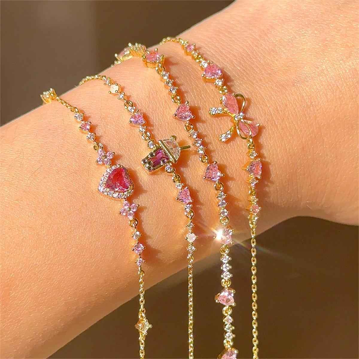 Gold-tone rhinestone bow and heart charm bracelets with pink stones on wrist