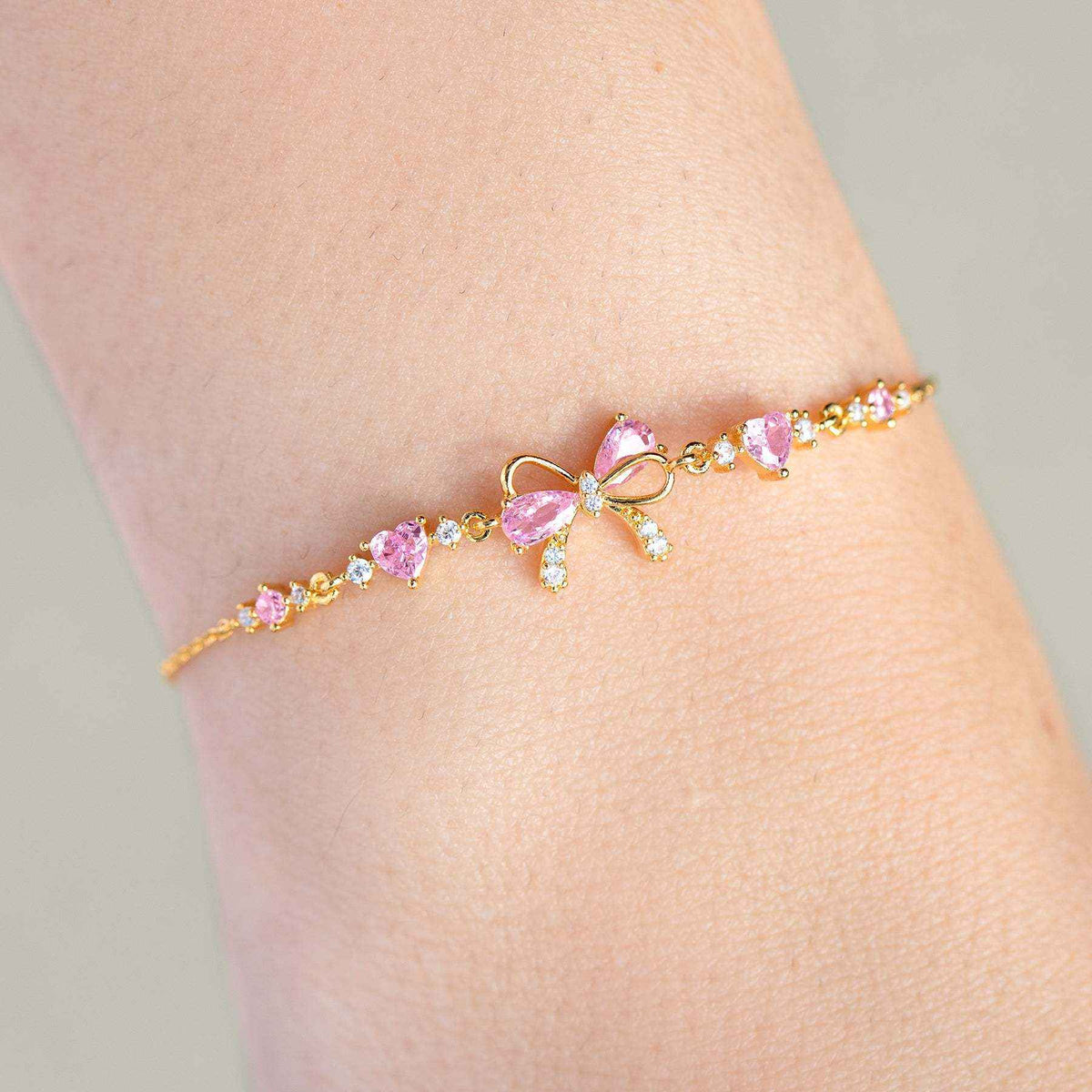 Gold-tone rhinestone bow bracelet with pink heart stones and small clear accents