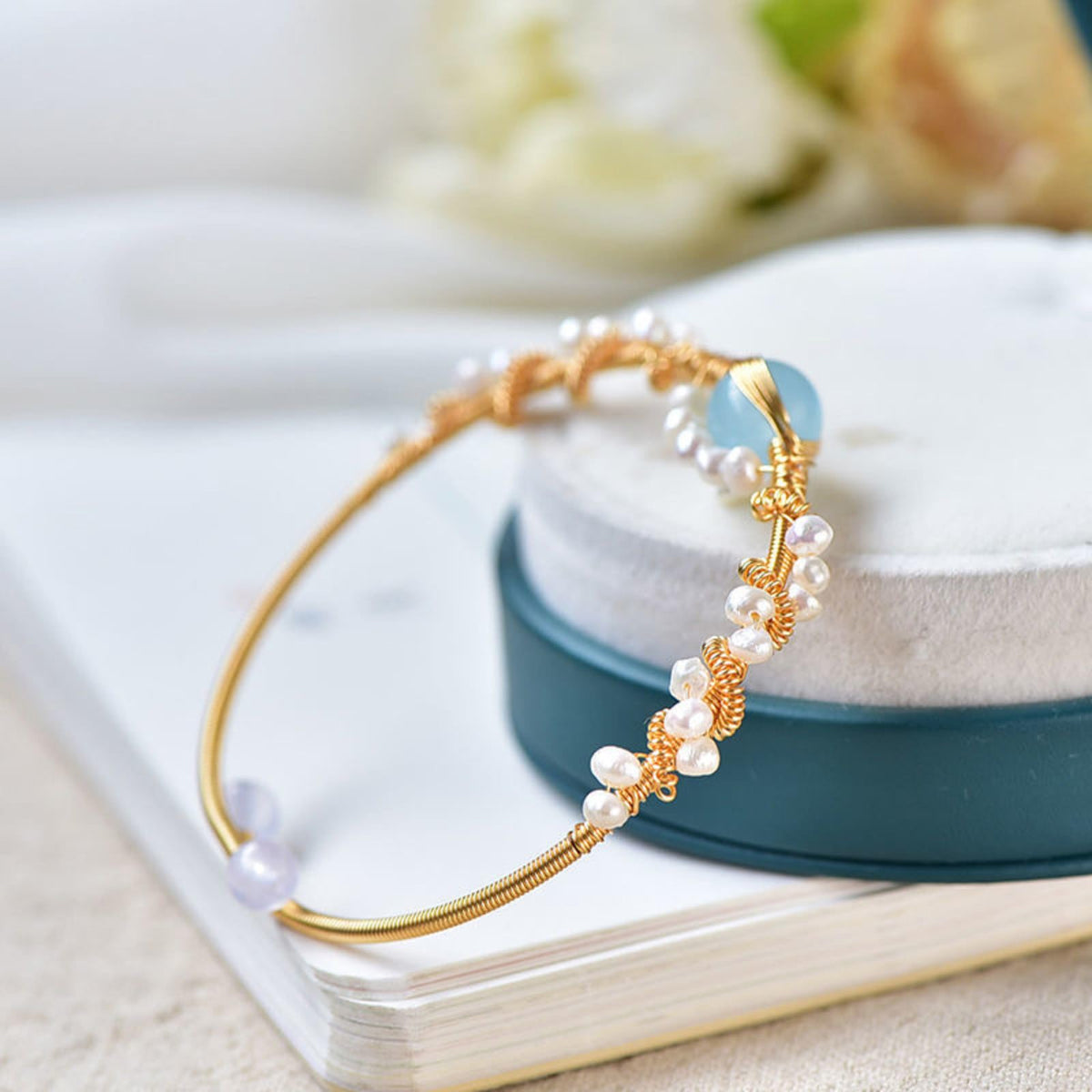 Gold pearl cuff bracelet with white beads and blue oval accents on braided band