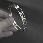 Silver stainless steel cuff bracelet held in hand; engraved cursive name on slim band