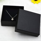 Silver-tone pendant chain with round stone, shown inside a black jewelry box
