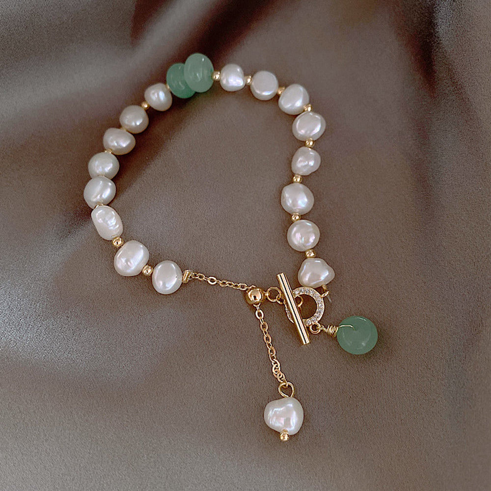 Freshwater pearl bracelet featuring white pearls, green bead accents, and gold charm dangles