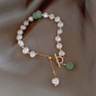 Freshwater pearl bracelet featuring white pearls, green bead accents, and gold charm dangles