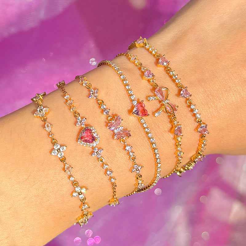 Gold-tone rhinestone bow and heart chain bracelets stacked on wrist with pink stones